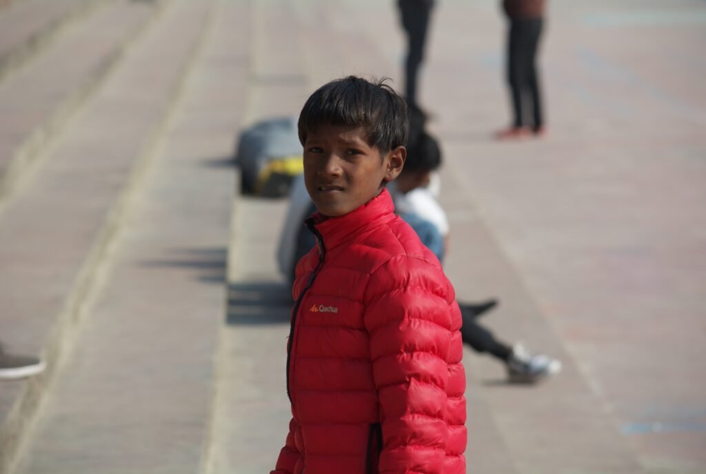 a brown, 12 year old male kid, wearing a red jacket is looking straight in the camera with an annoying expression on his face.
